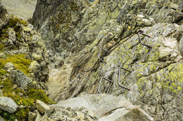 Metallschnallen und Kette, die Ihnen helfen, einen steilen und schwierigeren Teil des Weges in den Bergen zu überwinden, der durch eine Rinne führt. - Foto, Bild