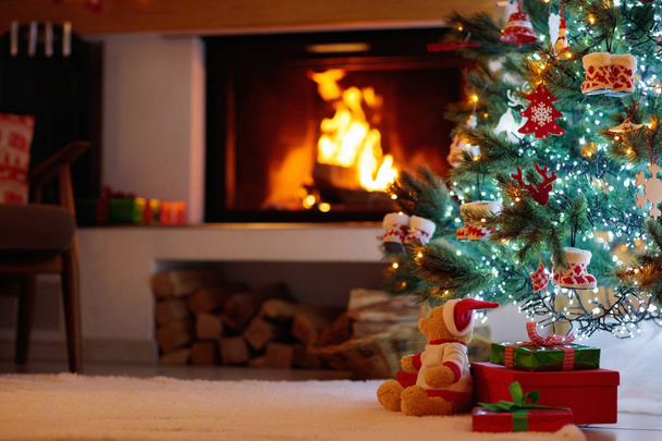 Christmas tree with presents at decorated fireplace. Family celebration of winter holidays. Living room interior with open fire place and Xmas tree with gifts for kids. - Foto, imagen