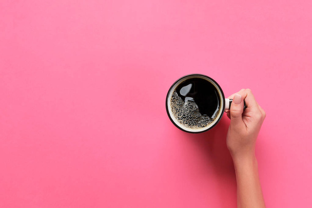 Mano de mujer de estilo minimalista sosteniendo una taza de café sobre fondo rosa. Piso tendido, vista superior. - Foto, imagen
