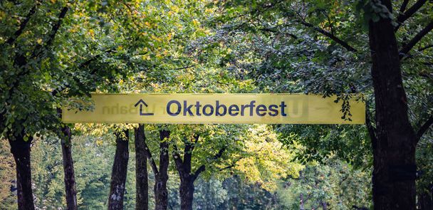 Οκτόμπερφεστ, Βαυαρία, Γερμανία. Είσοδος κατατοπιστική είσοδος στον εκθεσιακό χώρο, κίτρινο, κείμενο Οκτόμπερφεστ, πράσινα δέντρα φόντο - Φωτογραφία, εικόνα