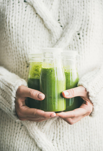 Winter seasonal smoothie drink detox. Female in light knitted sweater holding bottles of green smoothie or juice in her hands - Fotó, kép
