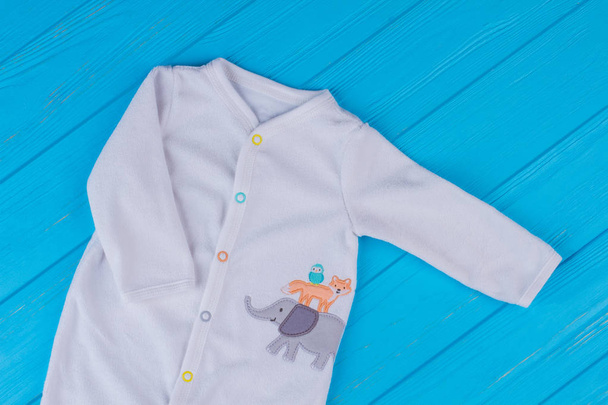 weißer Baby Pyjama aus weicher Wolle mit Print. blauer Holz Hintergrund. - Foto, Bild