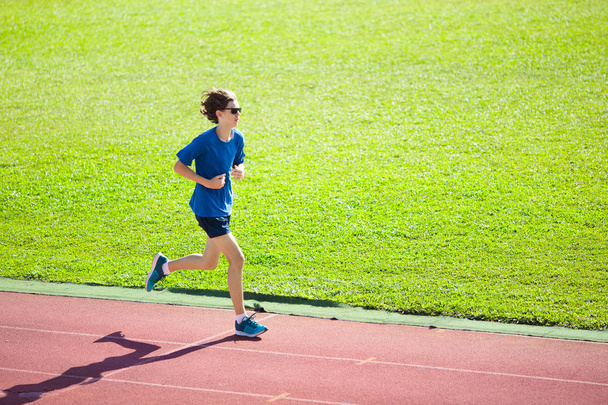 Boy running on outdoor stadium race track. Teenager sprinting during athletics training. Teenage kid jogging. Healthy sport for school kids. Young man enjoying summer run. Active exercise. - Photo, Image