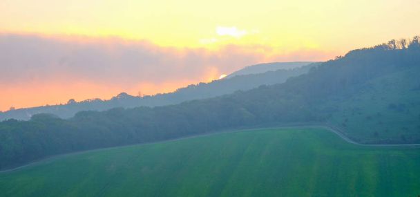 Britský venkov řádkům stromy a kopce slunce za kopcem a dávat oranžové záře na obloze, při pohledu přes rozsáhlé zelené oblasti Firle vesnice, Sussex, Anglie, Velká Británie,  - Fotografie, Obrázek