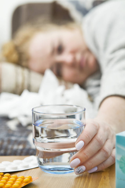 Młoda kobieta cierpi na bóle głowy, przeziębienia i grypy trzyma szklankę wody - Zdjęcie, obraz