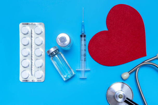 Medical, medicine stethoscope, syringe, injection and pills on blue background. Health care or illness. Cardiology heart treatment - Photo, image