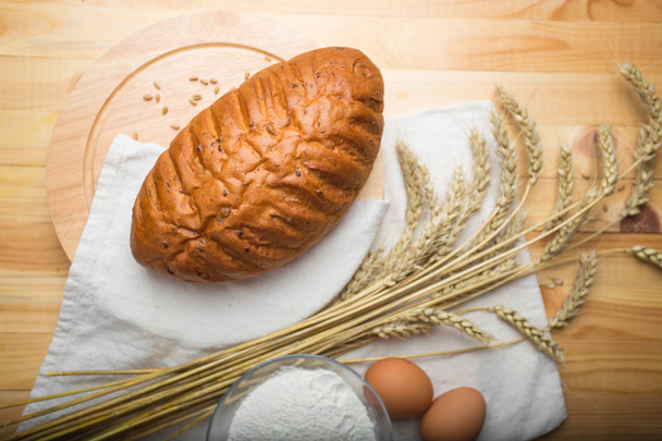 freshly baked bread, wheat, eggs and flour on a white linen cloth over a light wooden background. Still life cooking, kitchen table. - Photo, Image