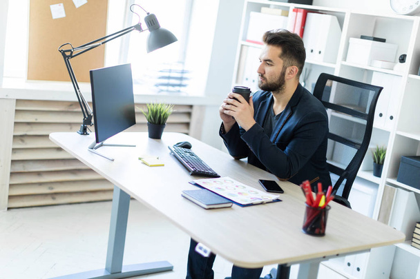 ein junger Mann arbeitet im Büro am Computer und hält ein Glas Kaffee. - Foto, Bild