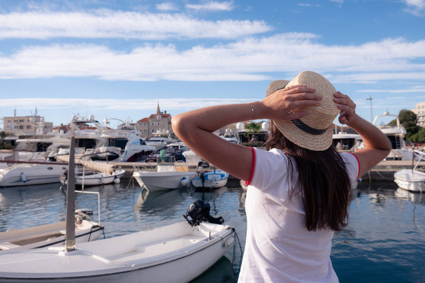 Beautiful young woman in hat standing close to the boats at Mediterranean city marina port. - Zdjęcie, obraz
