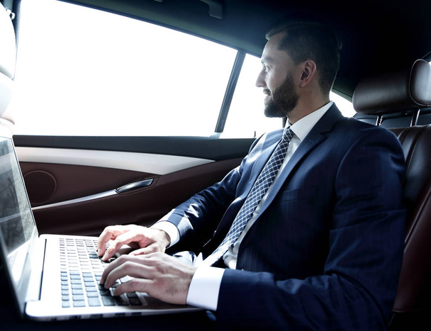 Businessman typing text on laptop while sitting in car - Фото, изображение