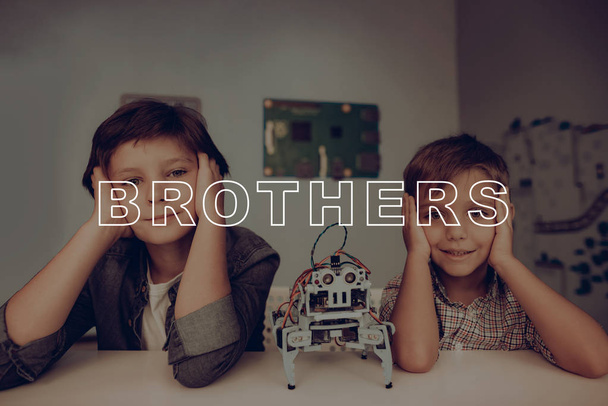 Two Young Brothers Are Posing. Grey Robot On The Table. Innovation Technology. Smart Kids. Artifical Intelligence. Educational Weekend Activity. Confident Children Stare. Childhood Concept. - Foto, Imagen