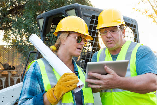 Mannelijke en vrouwelijke werknemers met technische blauwdrukken en Computer Tablet praten op bouwplaats - Foto, afbeelding