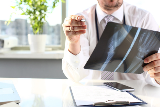 Мужчина врач держать в руке серебряную ручку и смотреть на рентген
 - Фото, изображение