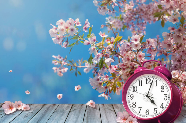 Óra és cseresznye virágok tavaszi fából készült asztal - napvilág megtakarító idő fogalma - Fotó, kép