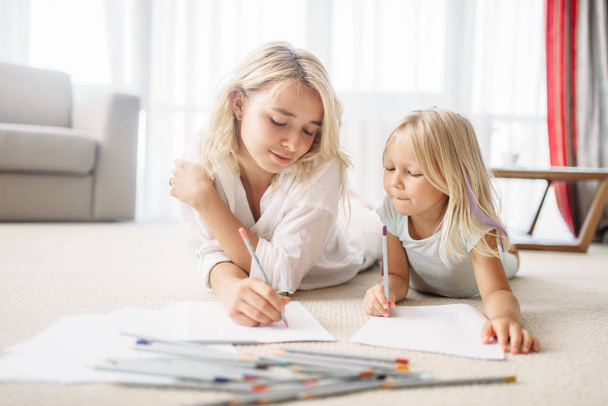 Mother and daughter draw with pencils lying on the floor. Parent feeling, togetherness - Foto, Bild