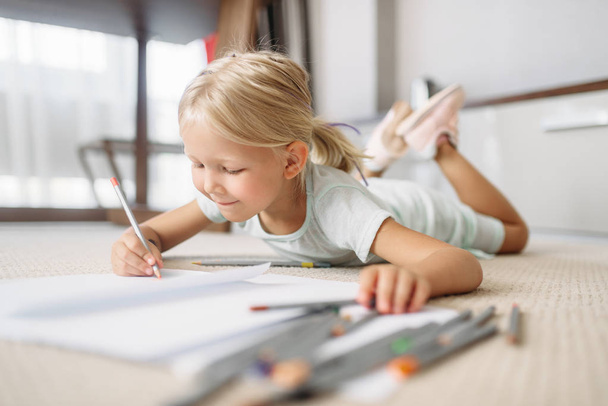Una niña dibuja tirada en el suelo en casa. Una infancia verdaderamente despreocupada, tiempo feliz
 - Foto, imagen
