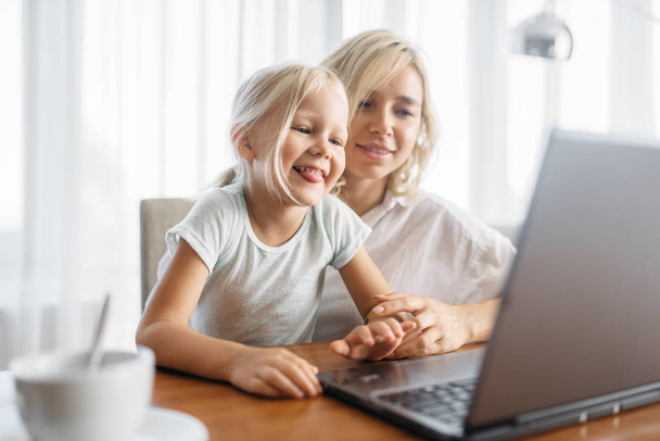 Glimlachen van moeder en kind maakt gebruik van laptop thuis. Bovenliggende gevoel, saamhorigheid, gelukkige familie - Foto, afbeelding