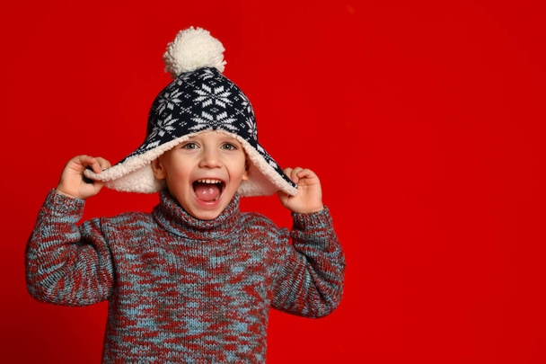 child boy in knitted hat and sweater having fun over colorful red  background. - Fotografie, Obrázek