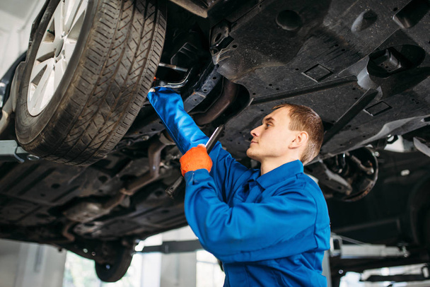 Mechanic with lamp checks car brake hoses, repair station. Tire service, vehicle maintenance - Фото, изображение