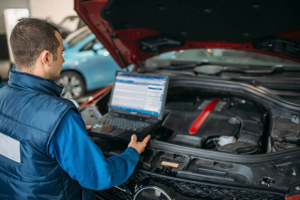 Engineer with laptop makes computer diagnostics of the car engine in auto-service. Vehicle wiring inspection - Photo, Image
