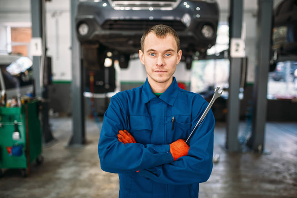 Mechanic with a wrench in hands, car on the lift on background, repair station. Tire service, vehicle maintenance - Fotoğraf, Görsel