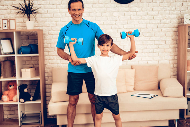 Sports for Kids. Boy with Dumbbells in Hands. Boy with Dumbbells in Hands. Sport at Home. Health Concept. Healthy Lifestyle. White Sofa. Lying on Floor. Male Trainer. Helping Little Boy with Dumbbells - Foto, afbeelding