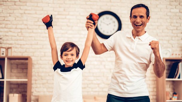 Boy Standing Hands Up. Sport at Home. Warm Up in Quarter. Tablet in Hands. Boxing Gloves. Doing Sports. Man and Boy Train at Home. Child in Boxing Gloves in Apartment. Little Boxer Champion. - Fotoğraf, Görsel