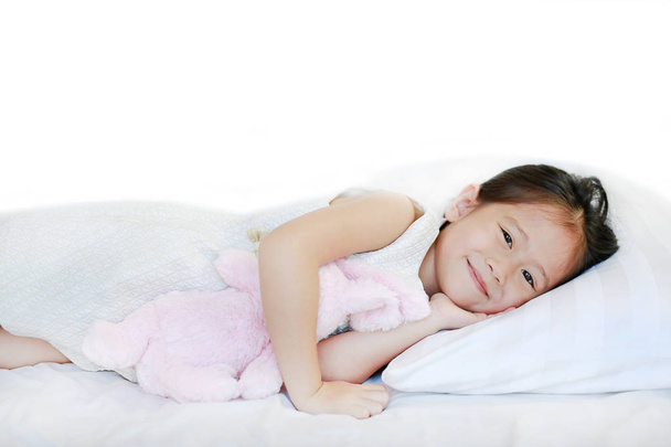 Portrait of a sweet smiling little Asian girl lying on bed in the morning with looking at camera. - Fotoğraf, Görsel