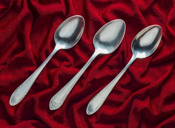 A set of three metal spoons on a red silk tablecloth. Top view. - Photo, Image