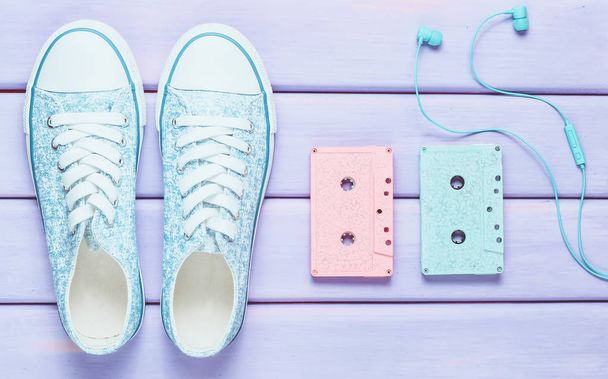 Casetes de audio de colores, auriculares, zapatillas de deporte zapatos sobre un fondo pastel púrpura. Tecnologías anticuadas. Vista superior. Puesta plana
. - Foto, Imagen