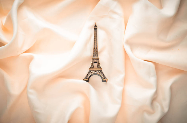 Estatuilla miniatura de la torre eiffel sobre fondo de seda blanca. Trend minimalism Souvenir from Paris (en inglés). Vista superior
. - Foto, imagen