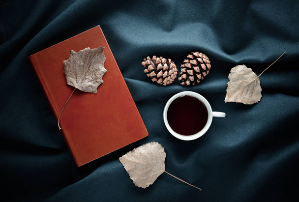 Őszi-téli hangulatot. Egy csésze tea, száraz levelek, fenyőtobozok a sötét lepedő. Felülnézet. Lapos feküdt. - Fotó, kép