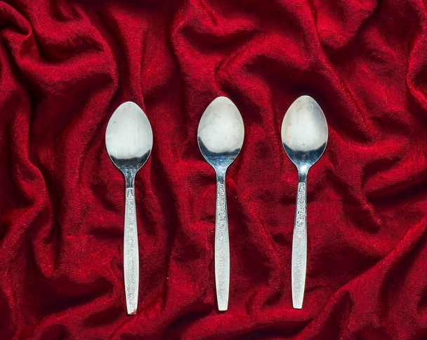 A set of three metal spoons on a red silk tablecloth. Top view. - Φωτογραφία, εικόνα