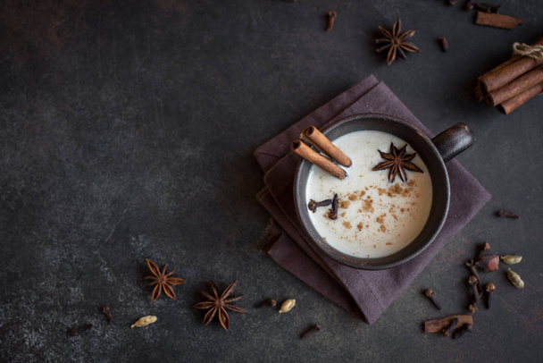 Traditional indian masala chai tea in ceramic cup with ingredients. Spicy black tea with milk on rustic dark background, copy space - Foto, immagini