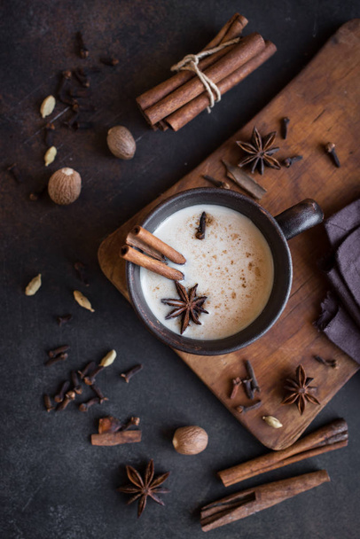 Traditional indian masala chai tea in ceramic cup with ingredients. Spicy black tea with milk on rustic dark background, top view. - Foto, immagini