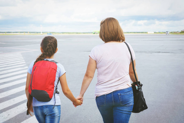 Mom with a bag and a daughter with a red backpack passengers go to the ramp of the plane on the airport field. - Photo, image