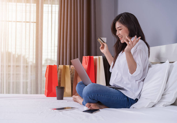 glückliche Frau benutzt Laptop für Online-Einkäufe mit Kreditkarte auf dem Bett - Foto, Bild