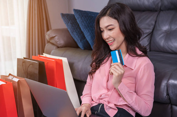 リビング ルームでのクレジット カードでオンライン ショッピングのためのラップトップ コンピューターを使用して幸せな女 - 写真・画像