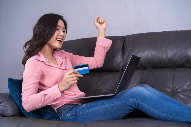 vrolijke vrouw u laptop gebruikt om succesvolle online winkelen met credit card in de woonkamer - Foto, afbeelding