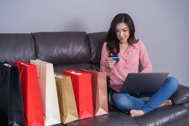 счастливая женщина, использующая ноутбук для онлайн-покупок с кредитной картой в гостиной
 - Фото, изображение