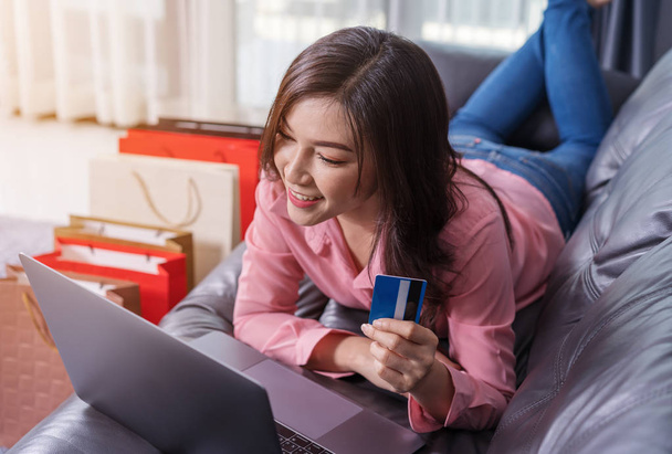 リビング ルームでのクレジット カードでオンライン ショッピングのためのラップトップ コンピューターを使用して幸せな女 - 写真・画像
