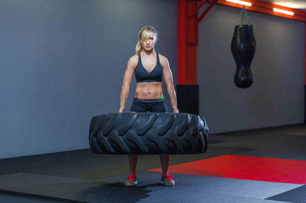 Fit female athlete working out with a huge tire, turning and carry in the gym. Crossfit woman exercising with big tire - Фото, зображення