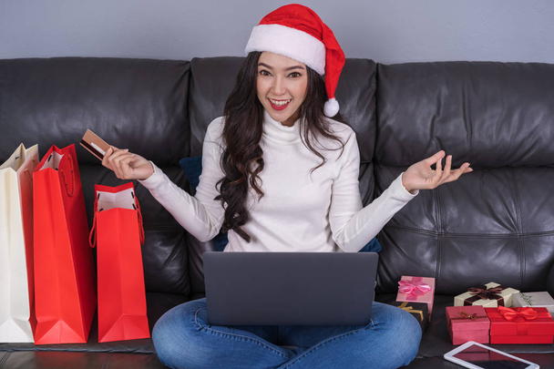 woman in santa hat shopping online for Christmas gift with laptop in the living room - Foto, Imagen