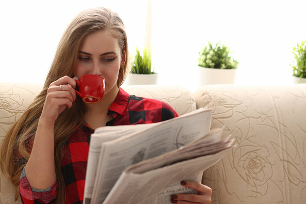 nő iszik kávé és olvasó ülni a kanapén - Fotó, kép