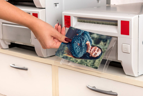 Woman taking a colored photographic print of a smiling pretty woman from a printer in a close up view of her hand and the machine - Photo, Image