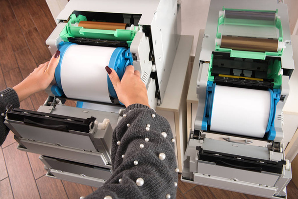 Mujer colocando un nuevo rollo de papel fotográfico en una impresora en un estudio fotográfico o imprenta en una vista cercana de sus manos
 - Foto, Imagen