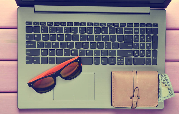 The concept of web work at a beach resort, freelancing. Laptop, sunglasses, purse on a violet color wooden table. Top view. - Photo, Image