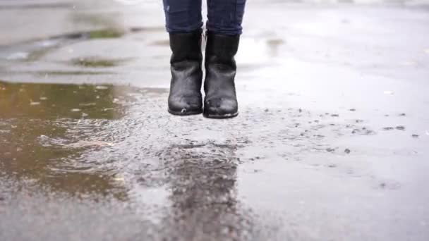 a girl in black leather boots stumbles in the autumn puddle during the rain - Footage, Video