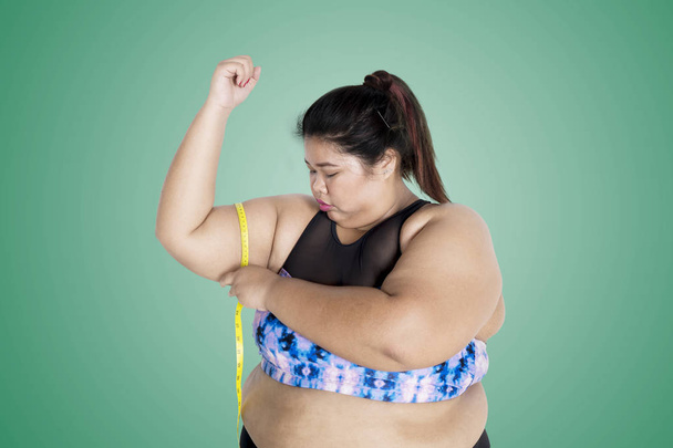 Picture of Asian fat woman wearing sportswear while measuring her upper arm with a measure tape - Фото, изображение