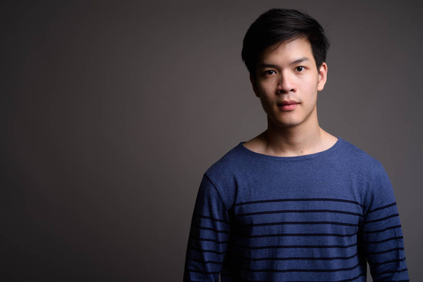 Young handsome Asian man against gray background - Foto, Imagem